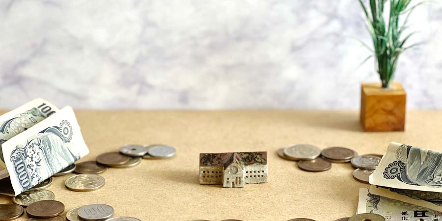 日本円の紙幣と硬貨に囲まれた小さな学校の模型。教育費や学費の負担をイメージした画像