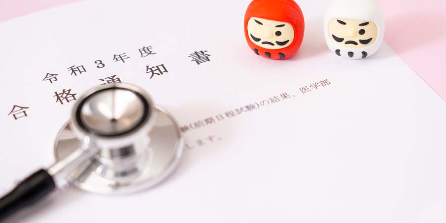 医学部合格通知書と聴診器、だるまの置物。医学部進学にかかる学費や教育ローンを連想させる画像
