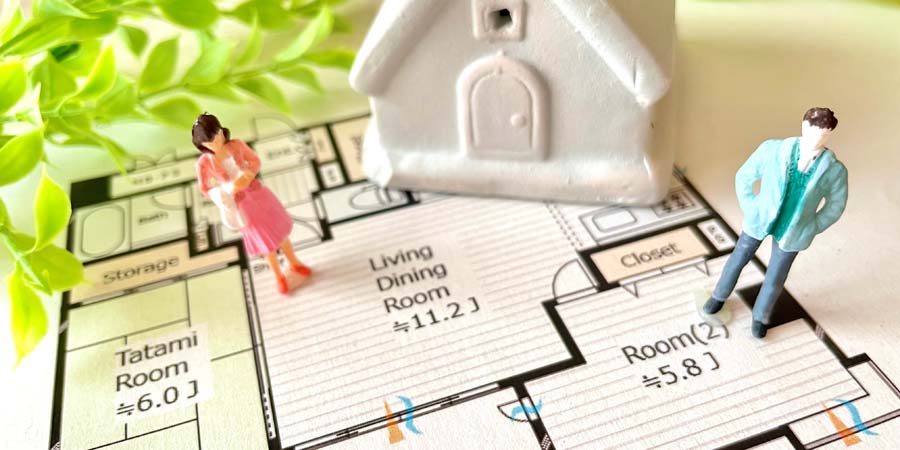 ミニチュアの男女と家の模型が、住宅の間取り図の上に配置されている