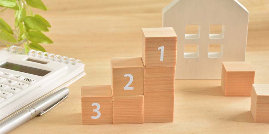 1〜3の番号が付いた木製ブロックが階段状に並び、背景に家の模型がある