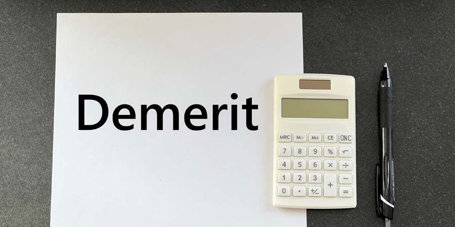 黒い背景のデスクに置かれた『Demerit』と書かれた白い用紙、電卓、黒いボールペン