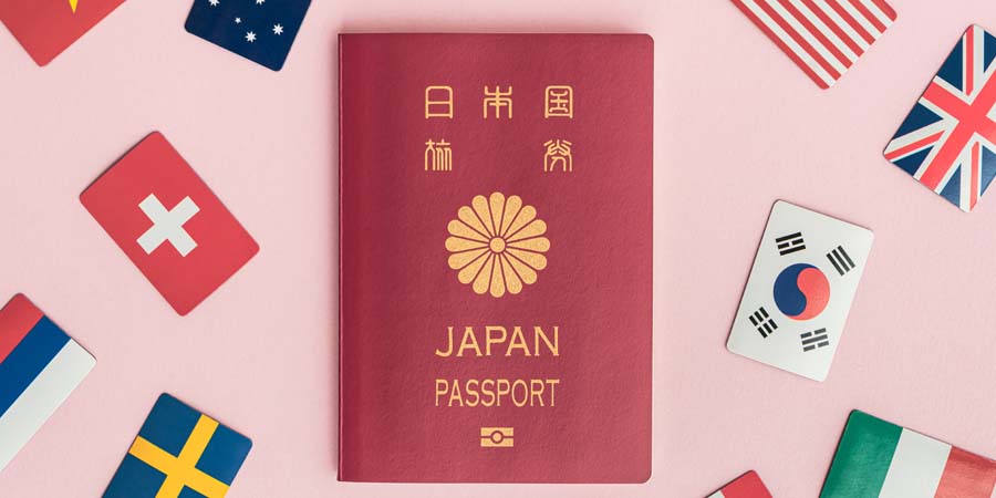 ピンク色の背景に置かれた日本のパスポートと、周囲に並ぶ、アメリカ、イギリス、韓国、カナダなど各国の国旗プレート
