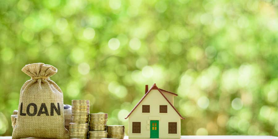 『LOAN』と書かれた麻袋と積み上げられたコインの横に、家のミニチュア模型が置かれている