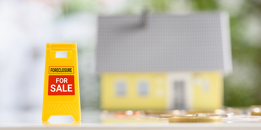 『FORECLOSURE』と『FOR SALE』と書かれた黄色の看板の奥に、ぼやけた家の模型がある