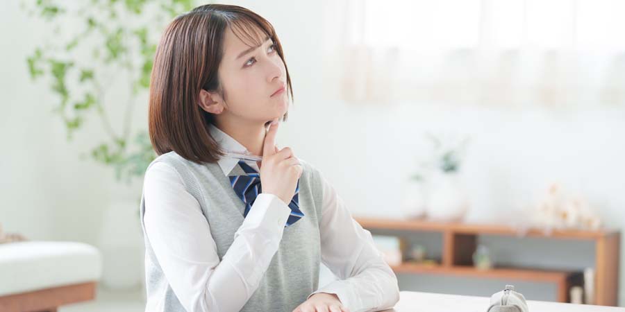 机に向かってノートを開き、進学や学費について考える女子学生の写真