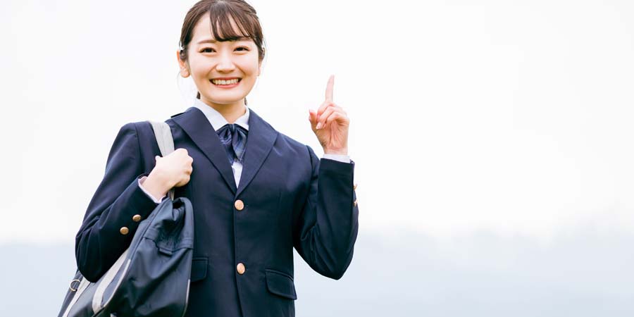 制服姿の女子学生が笑顔で指を立てている写真。進学の決意や希望を表すイメージ写真