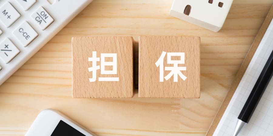 担保と書かれたブロックや電卓、家の模型を使って共不動産を担保にする融資方法を検討するイメージ写真