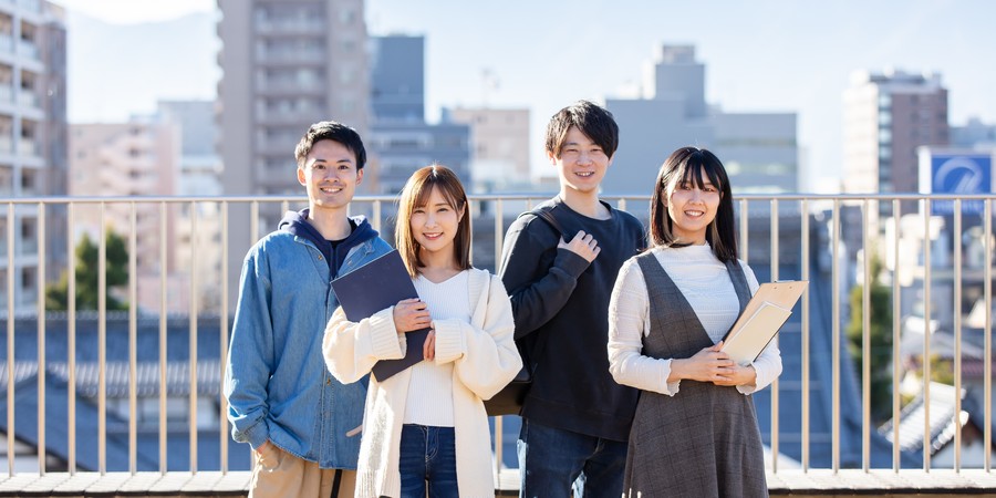 大学のキャンパスでノートを持って立つ大学生のイメージ写真