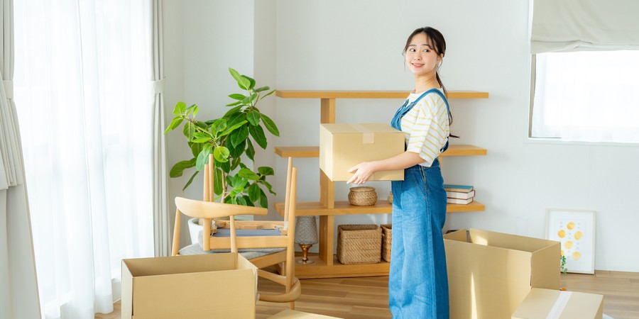 引っ越し作業中に段ボール箱を抱えて微笑む大学生の画像