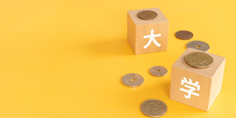 「大学」と書かれた木製ブロックとコインを並べた大学費用のイメージ写真