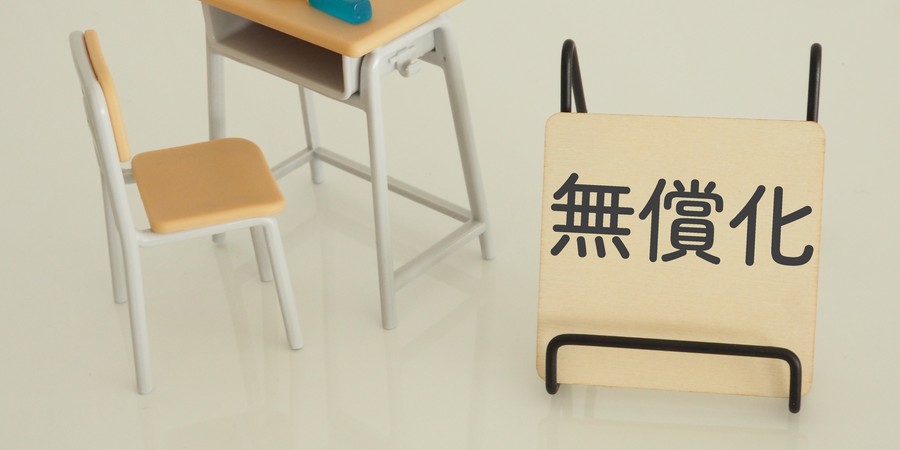 「無償化」と書かれたプレートと、本と文房具が置かれたミニチュアの学校机・椅子セットの画像