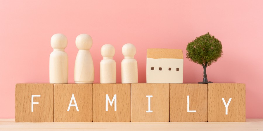 「FAMILY」と書かれた木製ブロックの上に、家族を表す木製人形4体・ミニチュアの家・木が並んでいる画像